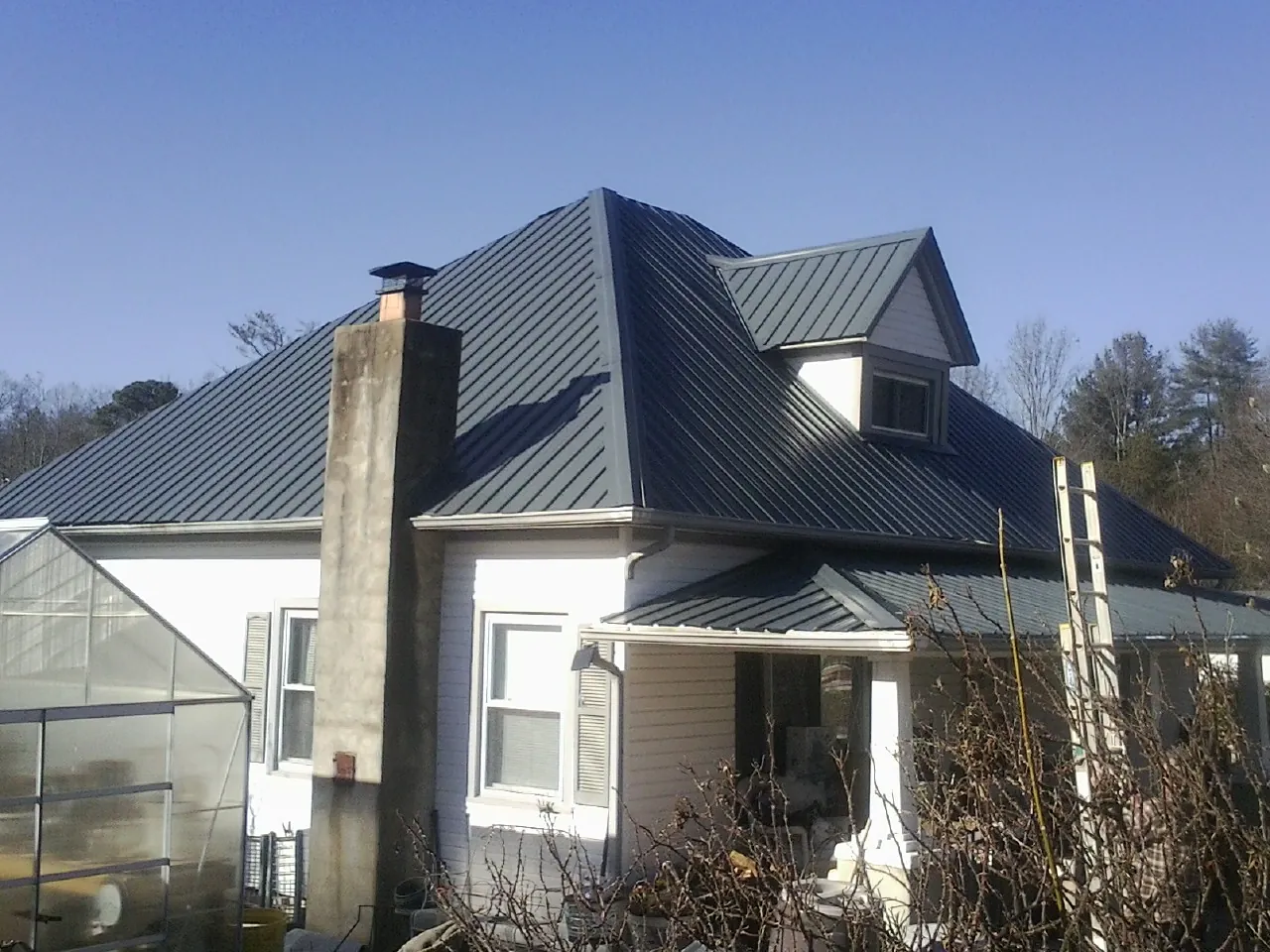 Dark blue standing seam metal roof on a white farmhouse with dormer — Slate & Tile Roof Repair by Roofing Brothers in Ballston Lake
