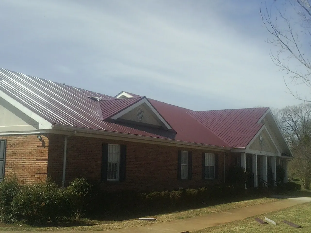 Red metal roof with gabled entries on a long brick building, from a Hail Damage Roof Repair job in Ballston Lake