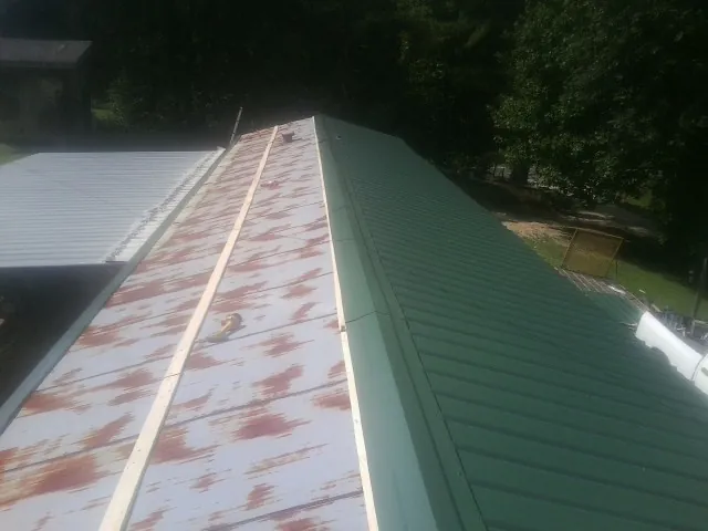 Old rusted panels beside newly installed green metal roofing — Wind Damage Roof Repair by Roofing Brothers in Ballston Lake