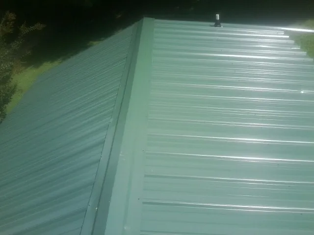 New green metal panels meeting at the ridge of a roof — Flat Roof Repair work by our crew in Ballston Lake