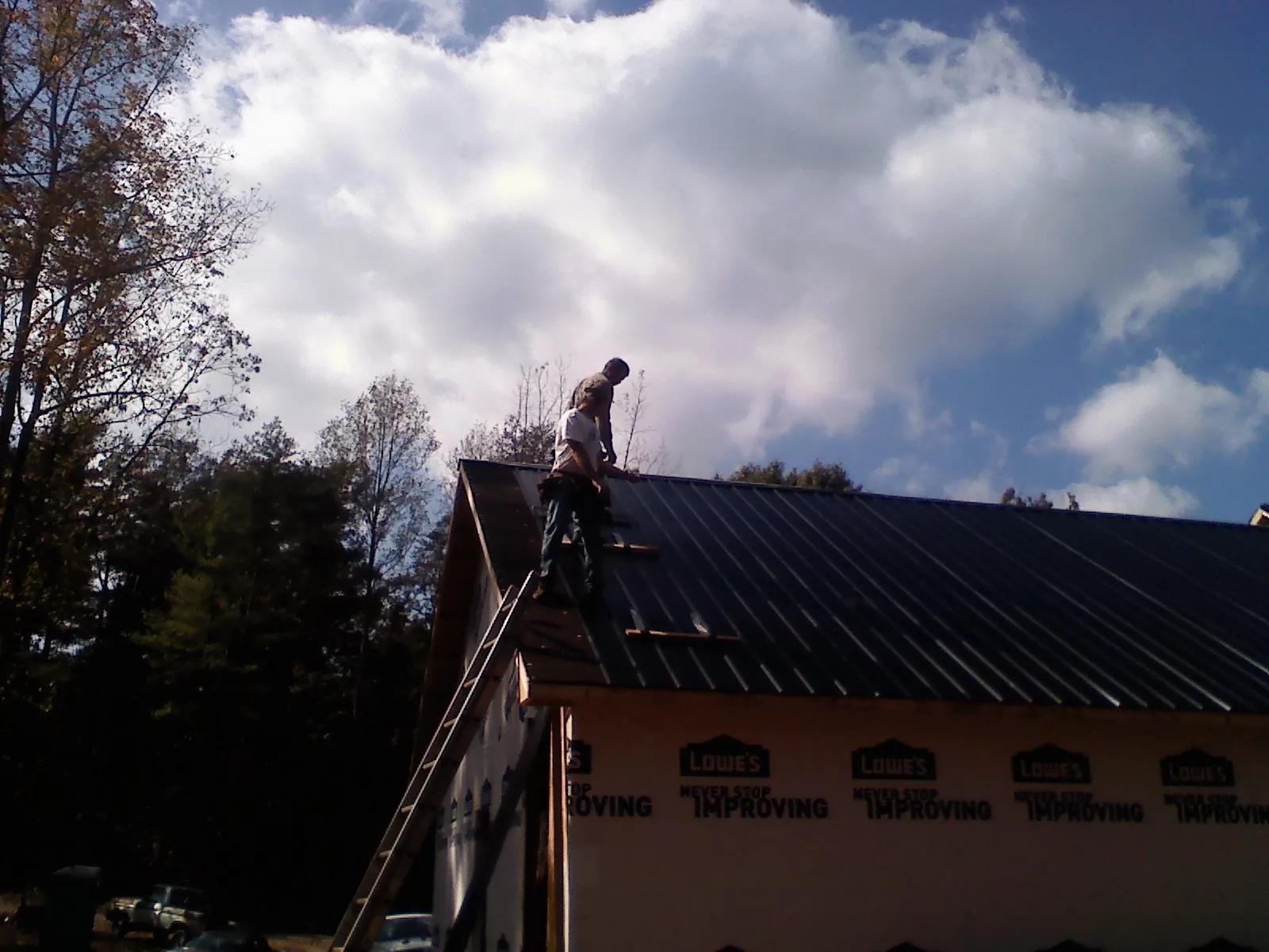Roofer fastening dark metal panels high against a cloudy sky, from a Roof Inspection job in Ballston Lake