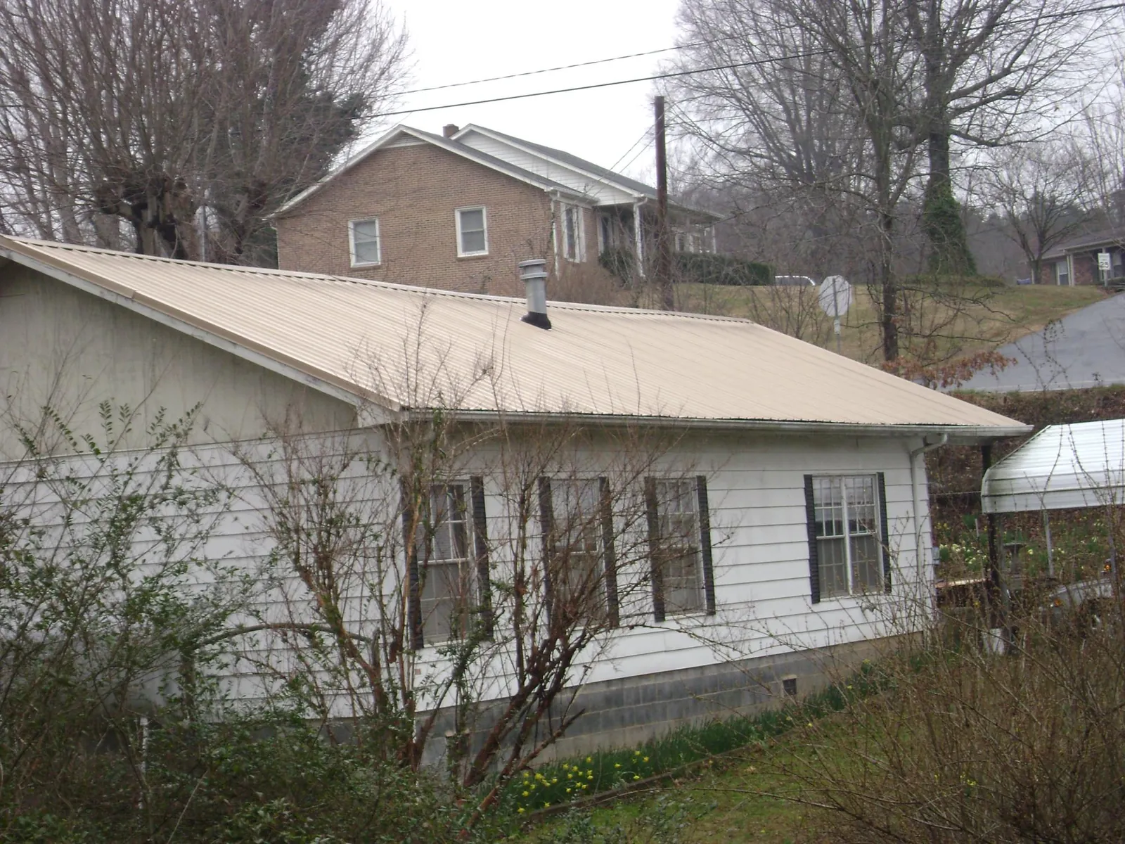 Tan metal roof on a white sided house set into a hillside — Commercial Roofing by Roofing Brothers in Ballston Lake