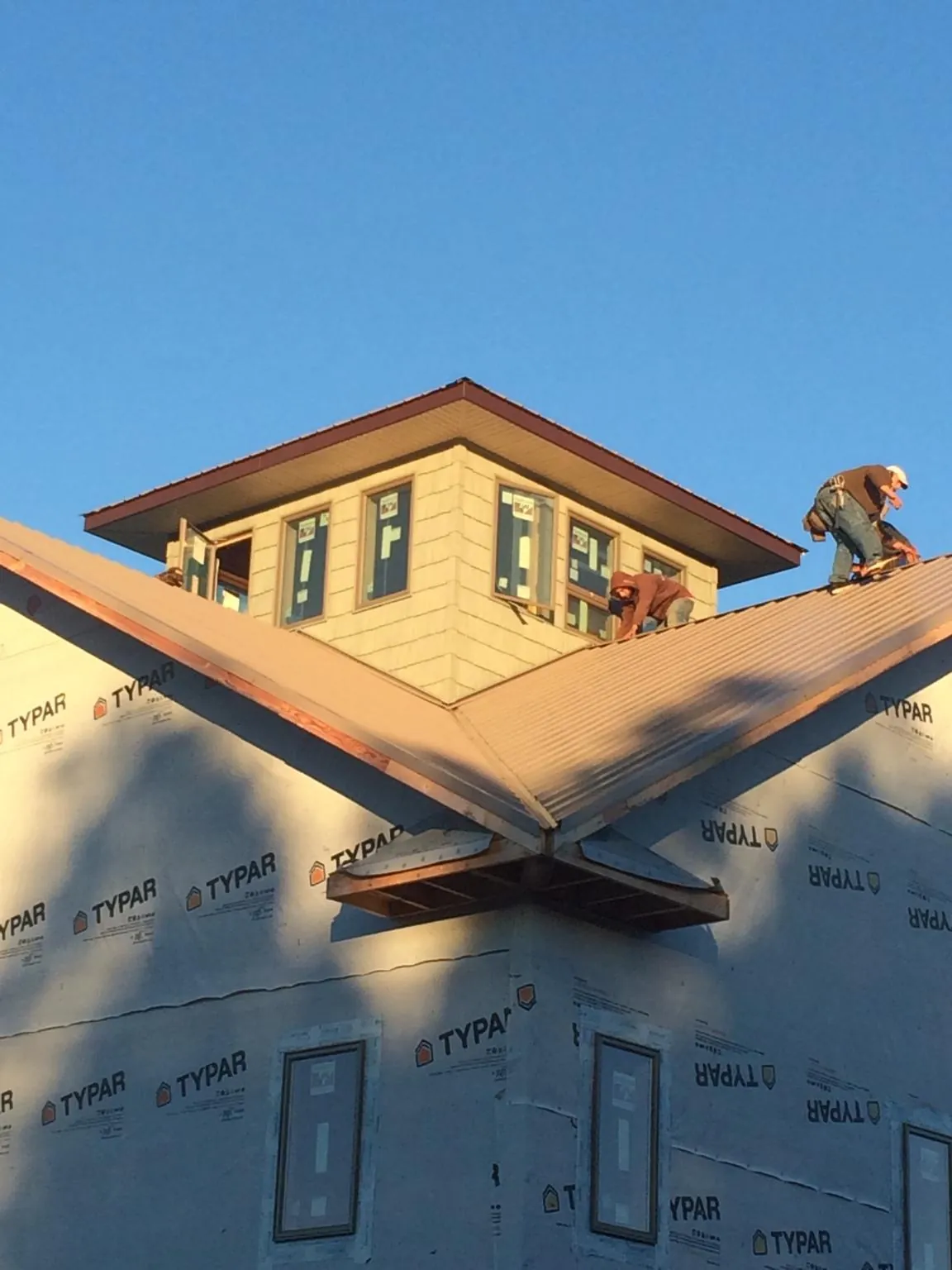 Roofers working around a rooftop cupola on a new metal roof at sunset in Ballston Lake